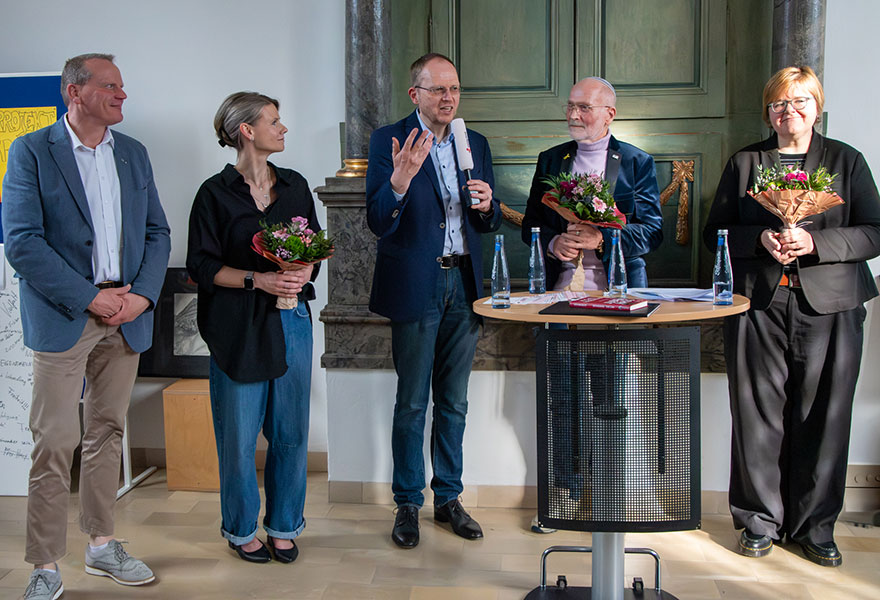 Die Beteiligten stehen im Halbkreis und haben Blumen in der Hand. Die Beteiligten stehen im Halbkreis und haben Blumen in der Hand.