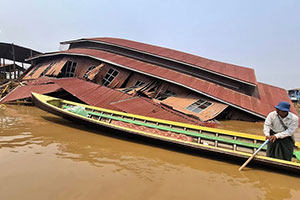 Ein Mann fährt mit einem Boot an einem zerstörten Haus vorbei. Ein Mann fährt mit einem Boot an einem zerstörten Haus vorbei.