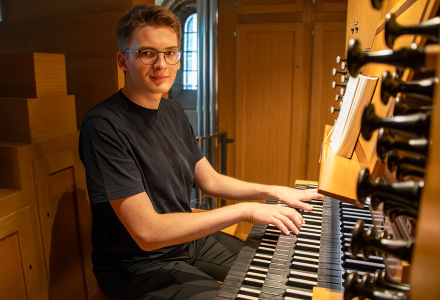 Julius Ennenbach sitzt an der Orgel und lächelt in die Kamera.