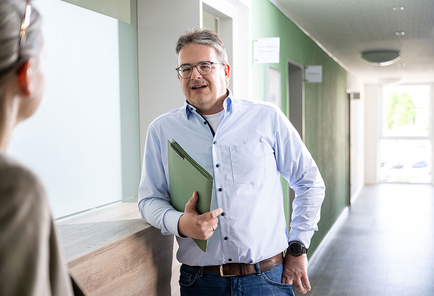 Sebastian Kohring hat eine Mappe in der Hand und unterhält sich.