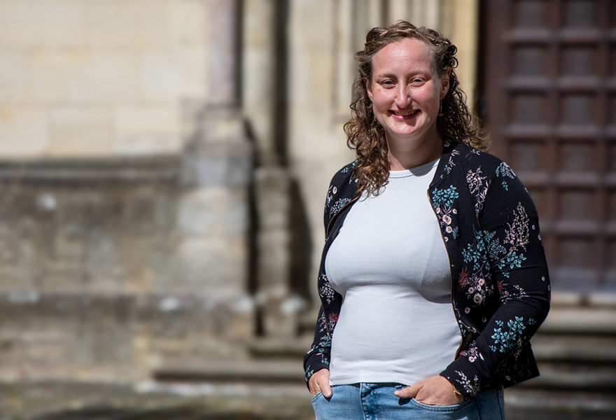 Sarah Behne steht am Billerbecker Dom und lächelt in die Kamera..