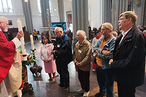 Ein Priester übergibt eine große Kerze an an eine Gruppe, die vor ihm steht.