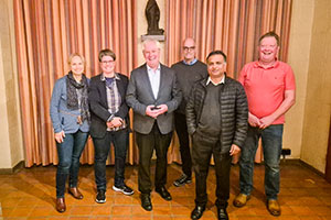 Sechs Personen stehen als Gruppe zusammen und lächeln in die Kamera.