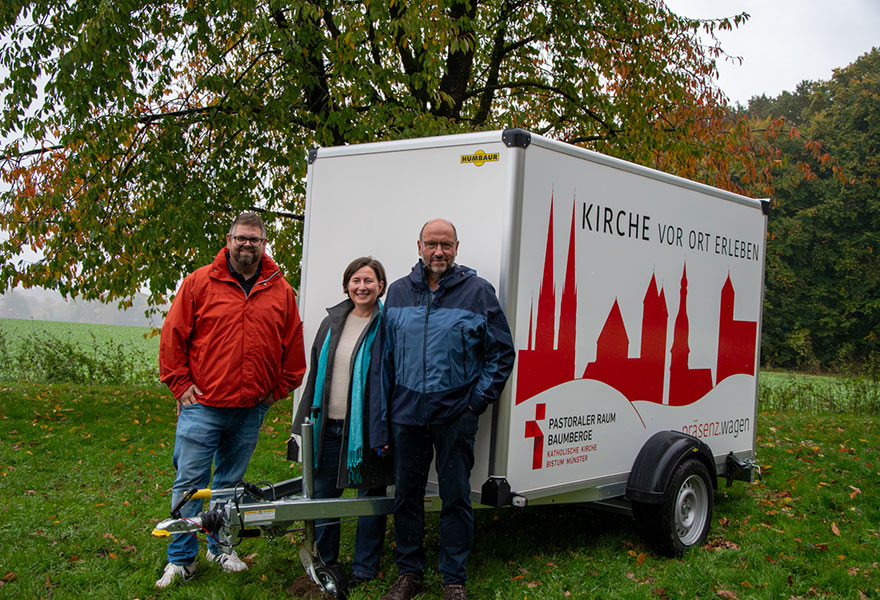 Andreas Groll, Nadine Vogt und Paul Eiersbrock stehen vor dem Autoanhänger, auf dem die Umrisse von vier Kirchen zu sehen sind.