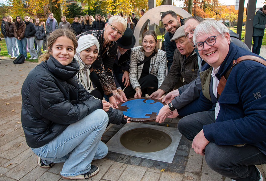 Organisatoren und Schülerinnen lassen gemeinsam mit dem Künsterpaar die Intarsie in den Boden ein.