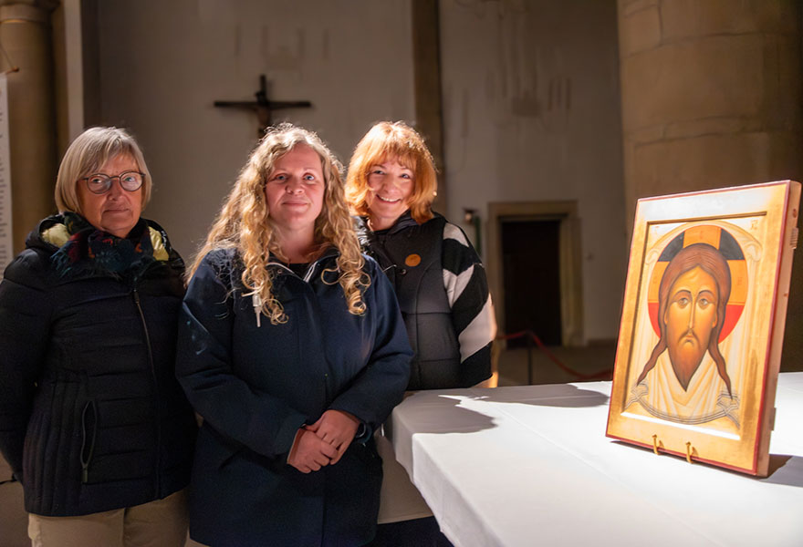 Auf dem Altar rechts steht die glänzende Ikone, daneben stehen drei Frauen und lächeln in die Kamera Auf dem Altar rechts steht die glänzende Ikone, daneben stehen drei Frauen und lächeln in die Kamera