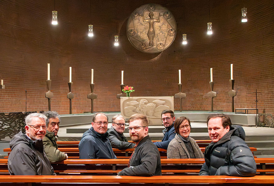 Die Beteiligten haben sich in die Kirchenbänke gesetzt, im Hintergrund ist der Altarraum zu sehen.