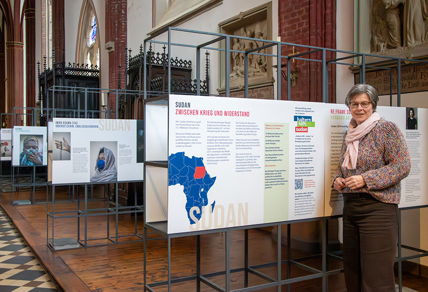 Gerburgis Sommer steht an einer Wand der Ausstellung, im Hintergrund erkennt man weitere Infotafeln.