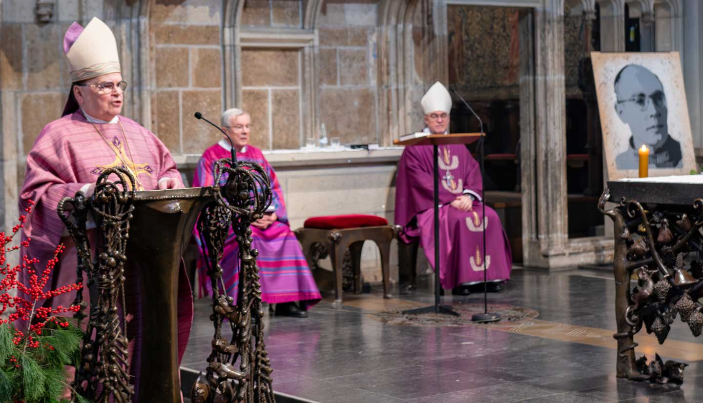 Bischof Meier steht am Ambo im Xantener Dom, rechts ist das Porträt von Karl Leisner aufgestellt.