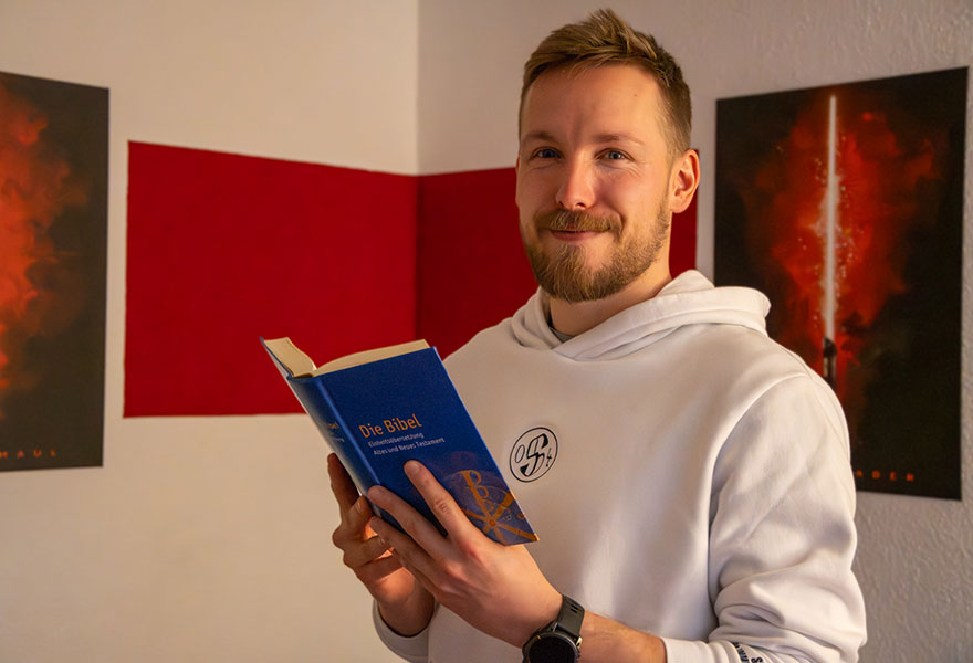 Max Kerkhoff hat eine Bibel in der Hand und lächelt in die Kamera.