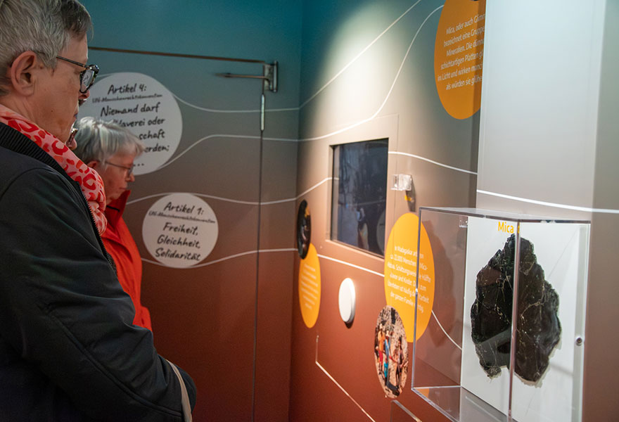 Besucherinnen schauen auf einen Monitor, im Vordergrund ist ein Stück Mica zu sehen.