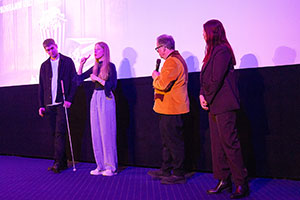 Vier Personen stehen vor der Leinwand und kommunizieren miteinander.