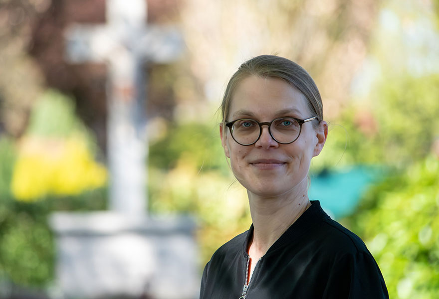 Porträt von Anke Rohde mit dem Kreuz auf dem Friedhof im Hintergrund