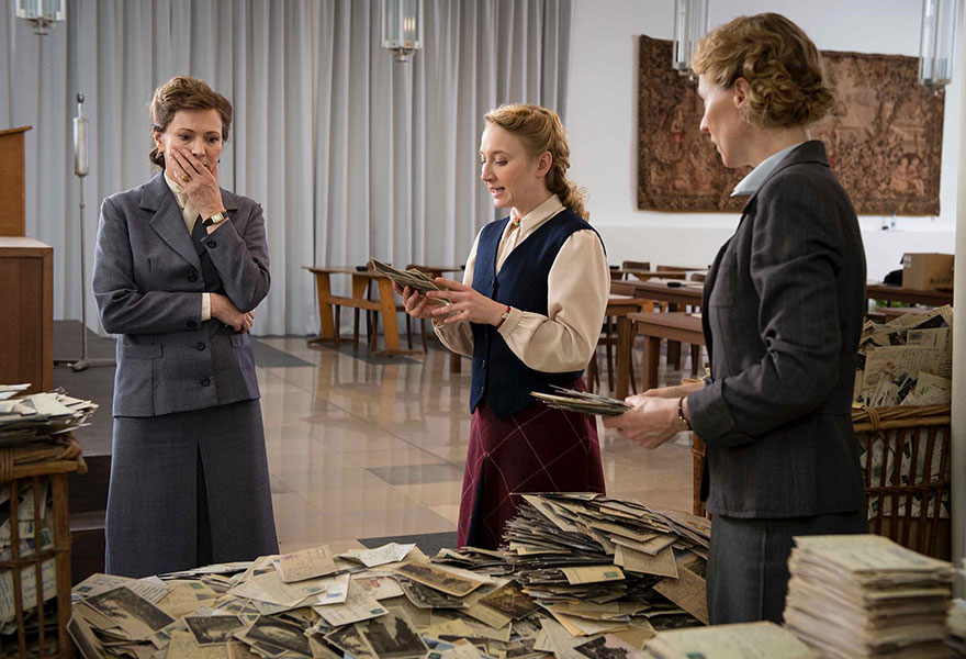 Filmszene, die drei Frauen zeigt, die auf eine große Anzahl von Postkarten schauen.