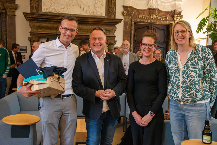 Vier Personen stehen nebeneinander und lächeln in die Kamera.