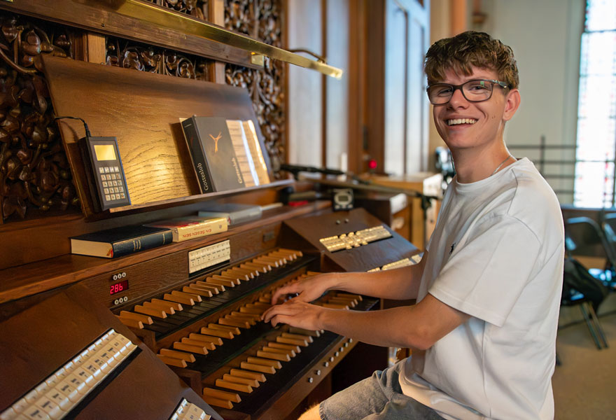 Ein junger Mann sitzt an der Orgel und lächelt in die Kamera.