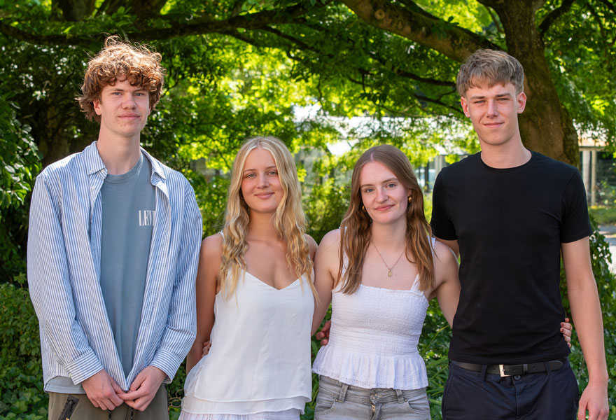 Vier junge Menschen stehen als Gruppe nebeneinander und lächeln in die Kamera. Vier junge Menschen stehen als Gruppe nebeneinander und lächeln in die Kamera.