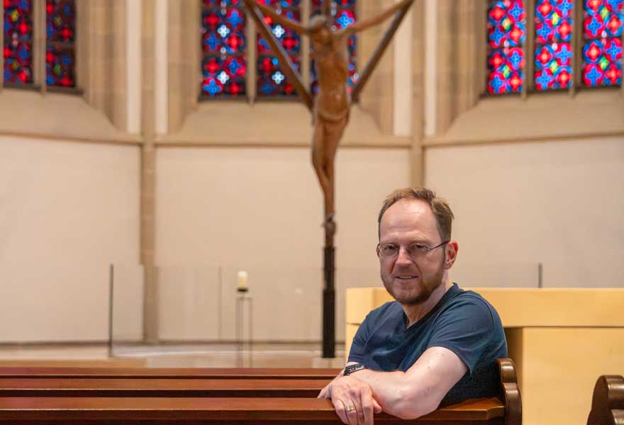 Jörg Hagemann sitzt in einer Kirchenbank, im Hintergrund das Coesfelder Kreuz