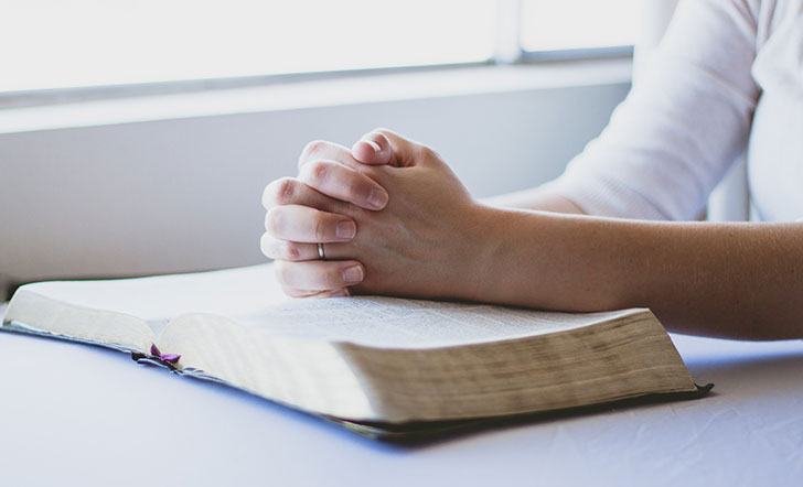Zwei zum Gebet verschränkte Hände liegen auf einer aufgeschlagenen Bibel.