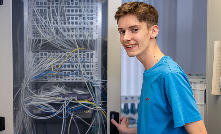 Ein junger Mann steht vor einem Schaltschrank mit Kabeln.