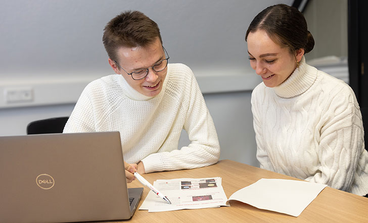 Zwei junge Menschen sitzen in einem Büro vor einem Computer.