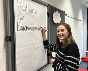 Die Auszubildende Sophie Messing steht mit einem Permanentmarker an einem Flipchart und schreibt: "Kaufleute für Büromanagement"