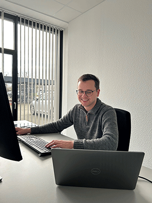 Stefan Dinkhoff sitzt an seinem Arbeitsplatz. Zu sehen sind Laptop, Desktop und Tastatur.