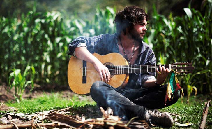 Ein junger Mann sitzt am Lagerfuer und spielt Gitarre
