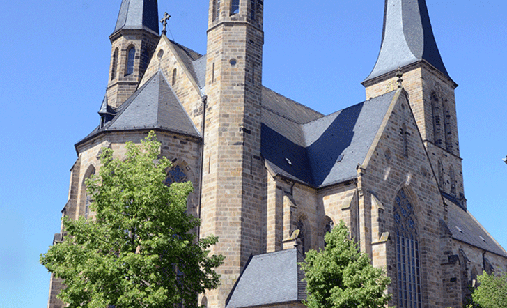 Kirchengebäude: St. Margareta in Wadersloh - Die Kirche St. Margareta in Wadersloh ist ein imposanter, gotisch geprägter Bau aus Sandstein mit markanten Doppeltürmen und einem hohen, spitz zulaufenden Dach. Die großen Maßwerkfenster, die kräftigen Strebepfeiler und die klar gegliederten Fassaden betonen die vertikale Ausrichtung des Gebäudes. Umgeben von Bäumen wirkt die Kirche zugleich eindrucksvoll und einladend.