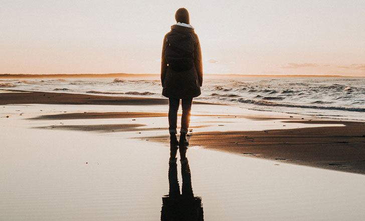 Eine Frau steht bei Sonnenuntergang an einem Strand