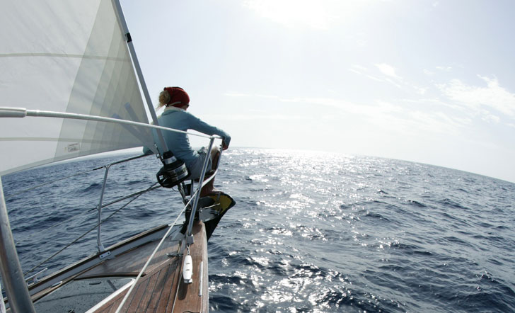 Eine Frau sitzt an der Spitze eines Segelschiffs und schaut in die Ferne.