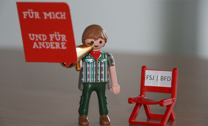 Ein Playmobilmännchen hält ein Megafon, aus dem eine Sprechblase mit folgendem Text kommt: "Für mich und für andere." Daneben ist ein regiestuhl mit der Aufschrift "FSJ/BFD" zu sehen.