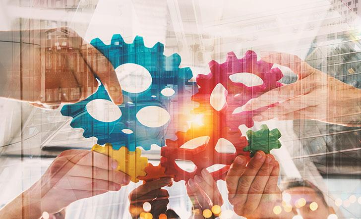 Symbolbild: Hände halten bunte Zahnräder, die ineinander greifen.