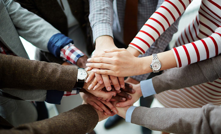 Mehrere Menschen haben ihre Hände in einem Kreis übereinandergelegt. 