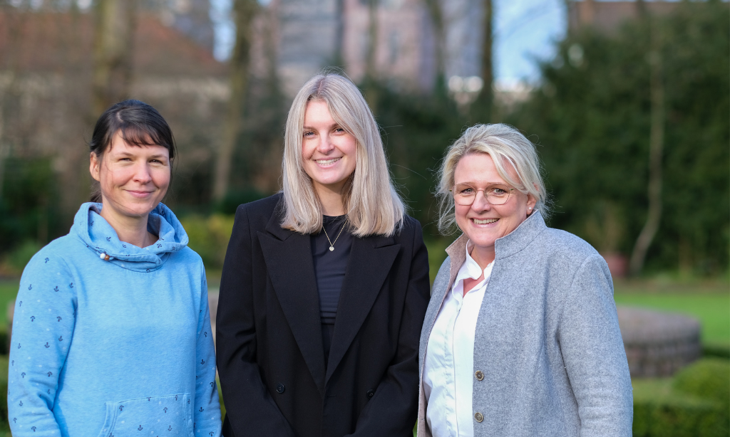 Drei Frauen stehen für ein Gruppenfoto nebeneinander,